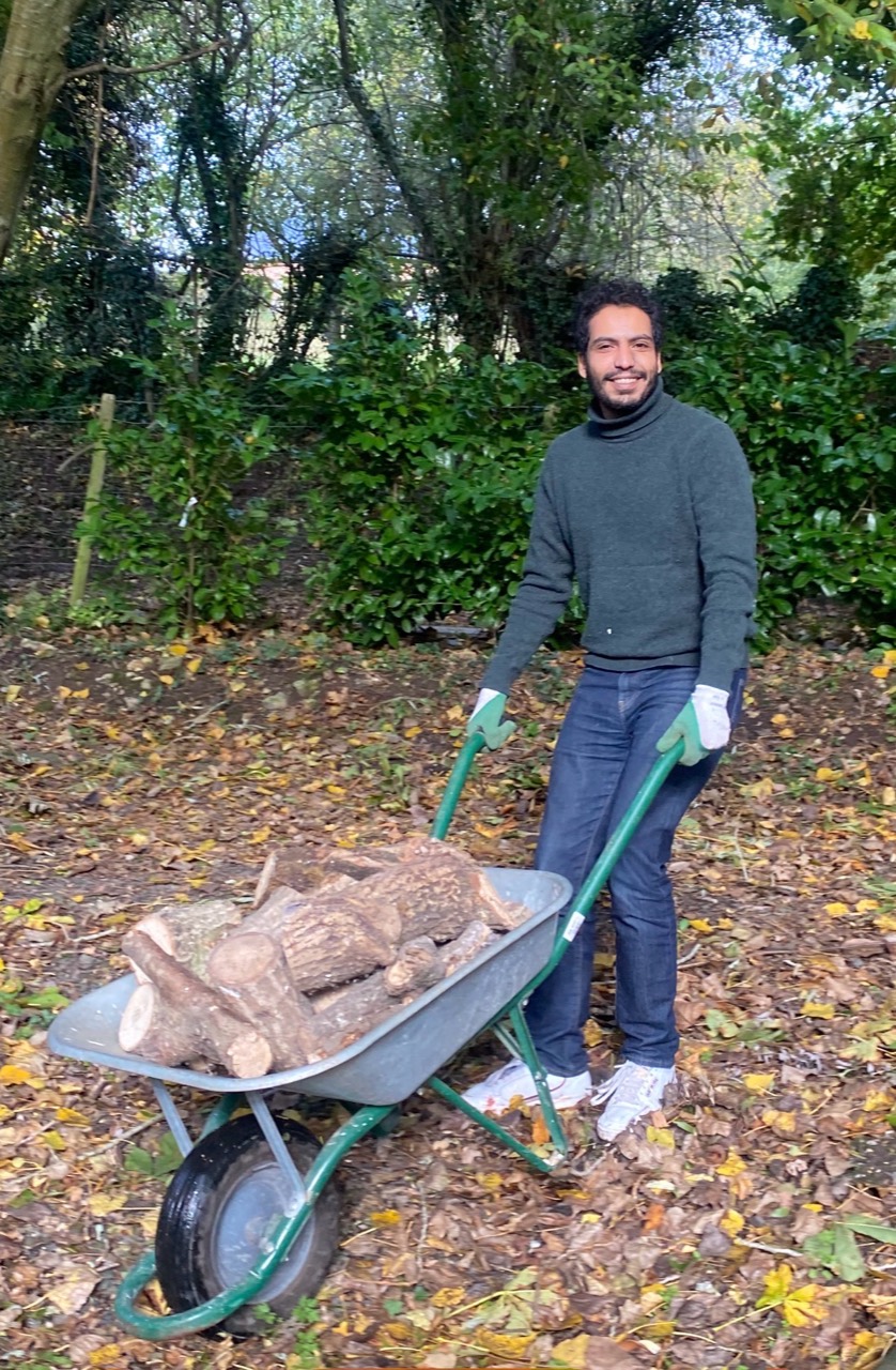 Soufiane Lemqari dans un jardin, avec une brouette chargée de bois.